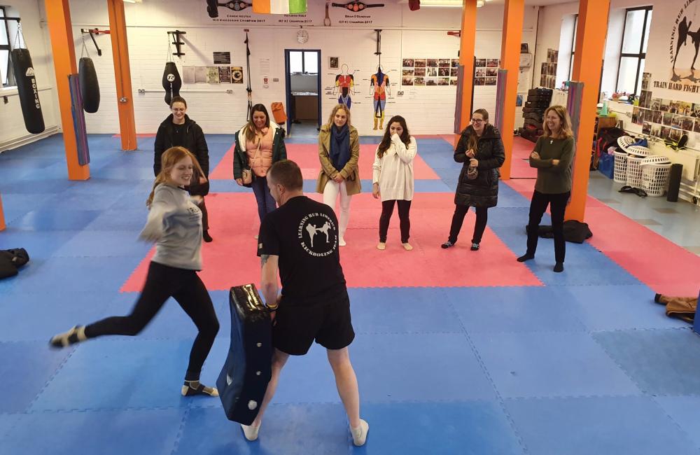 Woman kicking kickboxing pad held by Instructor Paul